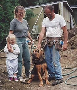 Tracker the Bloodhound sitting in the dirt with a lady, a man and a little girl