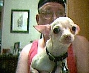 Spike the Chihuahua is being held by a man who is wearing a black hat and glasses
