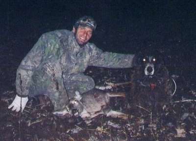 Whischo Vom Steinacher the Deutscher Wachtelhund dog is sitting in a field next to a dead dear. A man is leaning down next to the deer with his hand on top of the dog smiling, proud of their kill.