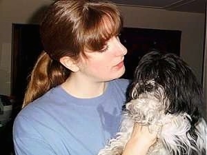 A red headed lady is holding up a black with white Kyi-Leo Dog inside of a house.