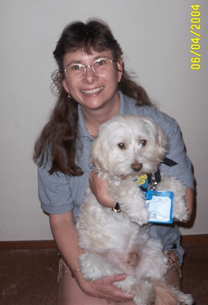 Kalani the Chin-Ocker being held in the lap of a lady who is kneeling on the floor and smiling