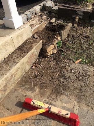 A stone walkway with dirt on it. There is a broom pushing the dirt to the grass.