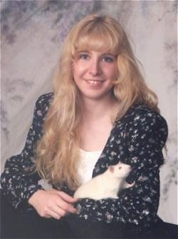 A white Rat is laying across the lap of a blonde haired Lady.