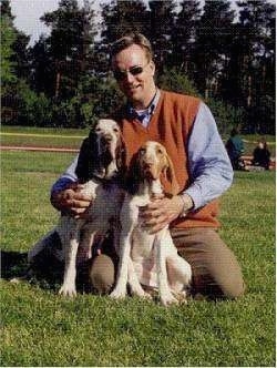 Two Bracco Italianos sitting in front of there owner who is kneeling on the grass and holding them close