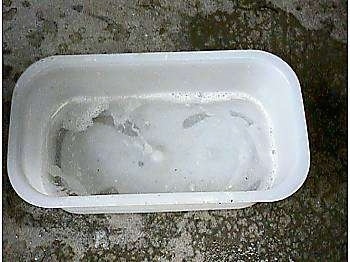 A white plastic water pan on a concrete surface. It has a few inches of very drooly bubbled water in it.