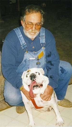 Babyface the Bulldog sitting on a tiled floor in front of her owner with her tongue hanging past her neck