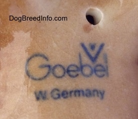 Close up - The underside of a brown and black porcelain Aussie puppy figurine. The logo of Goebel W. Germany is on the underside of the figurine.
