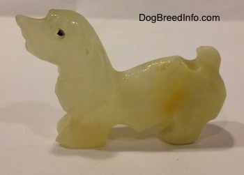 The left side of a stone Basset Hound figurine. The figurine has a black circles for eyes.