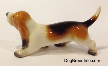 The left side of a black, tan and white ceramic Basset Hound figurine. The figurine lacks fine detail.