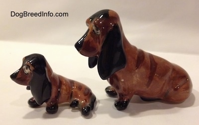 The left side of two, a mother and a puppy, brown and black ceramic Basset Hounds figurines. The figurines ears have fine details.