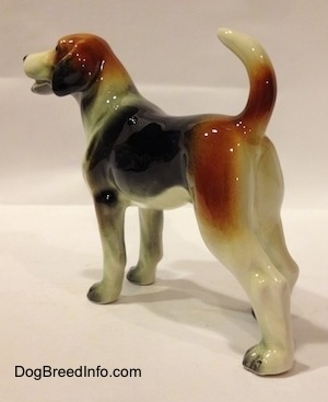 The back left side of a black, brown and white Beagle figurine. The ears of the figurine are detailed great. The dogs tail is high up in the air and the ears hang down low.