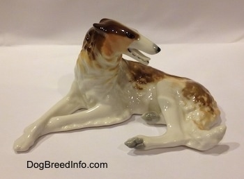 The left side of a brown, white and tan Vintage porcelain Lomonosov Borzoi figurine. The figurine has its mouth open. It has long legs and a long body with a long pointy muzzle and small ears.