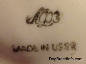 Close up - The underside of a Vintage porcelain Lomonosov Borzoi figurine. On the underside is an image of a Made in the USSR stamp and the Lomonosov logo.