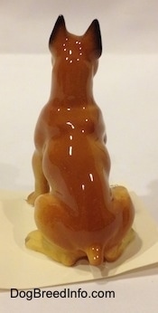 The back of a tan with black and white Boxer papa figurine. The figurine has a small tail.