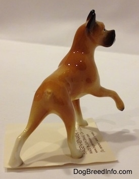 The back right side of a tan with black and white Boxer mama figurine. The tail of the figurine is indistinguishable from the body.