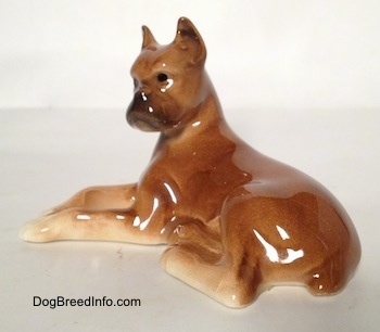 The back left side of a brown with tan Boxer dog figurine in a laying down pose. The figurine is very glossy.