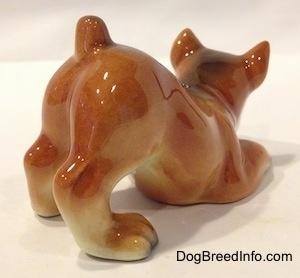 The back right side of a brown, black and white Boxer puppy in a play bow pose. The figurines paws have fine details.