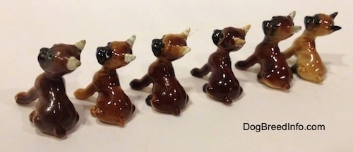 The back left side of a line-up of different color variations of a Boxer puppy figurine. All the figurines have black muzzles.