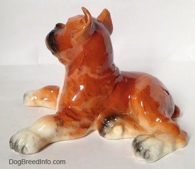 The left side of a fawn and white with black Boxer dog figurine in a laying pose. The paws of the figurine are very detailed.