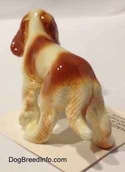 The back left side of a red and white Cavalier King Charles Spaniel figurine. The figurine has a long tail.