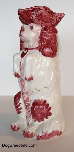 The front left side of a white and red Cavalier King Charles Spaniel porcelain water pitcher. The pitcher is glossy.