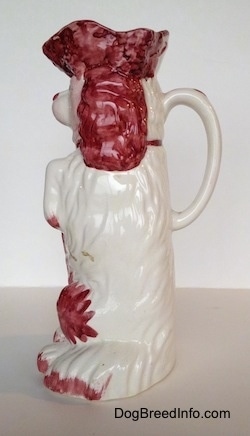 The left side of a white and red Cavalier King Charles Spaniel porcelain water pitcher. The handle on the back looks like a tail.