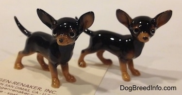 Two black with tan Chihuahua figurines that look different. The feet of the figurines are tan.