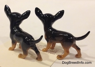 The back of two different looking black with tan Chihuahua figurines. The figurines are glossy.