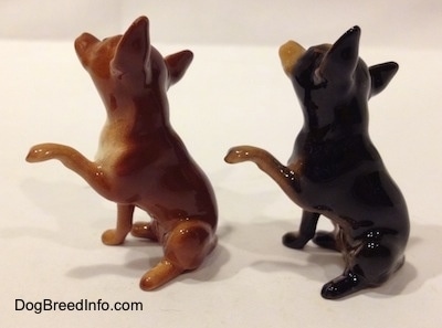 The left side of two Chihuahua figurines that are different and also have one paw in the air.