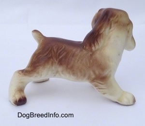 The right side of a brown and white ceramic Cocker Spaniel puppy figurine. The dog has long ears that hang down to the sides and a short cropped tail.