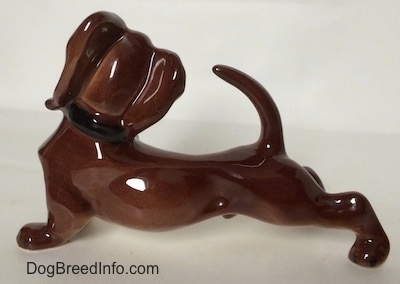 The left side of a figurine of a brown with white Dachshund figurine in a strecthing pose. The figurine has brown paws and short legs.