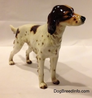 The front right side of a porcelain brown and white English Setter figurine. The figurine has long legs and small brown tipped paws.