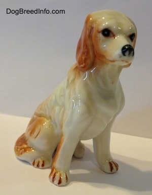 The front right side of a red and white bone china English Setter figurine. The figurine has long legs and small paws.