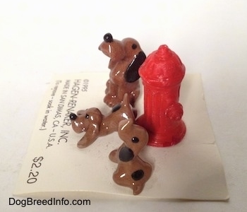 The left side of a set of Hound Dawg figurines around a red fire hydrant. All the figurines have black circles for eyes.
