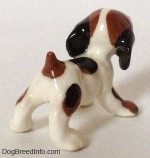 The back right side of a Hound dog figurine that is white with brown and black. The figurine has large paws.