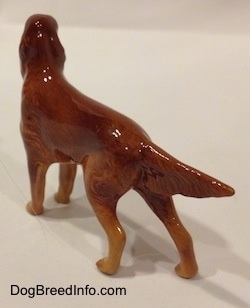 The back left side of a figurine of a brown Irish Setter. The figurine is glossy.