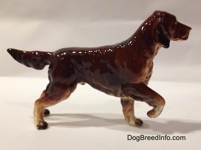 The right side of a brown with tan ceramic Irish Setter pointing figurine. The small paws of the figurine are brown and white.