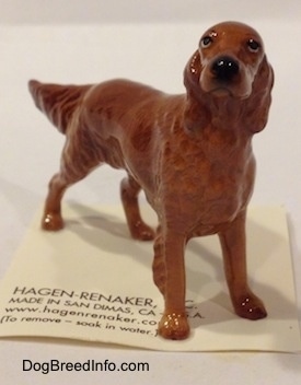 The front right side of a brown Irish Setter figurine. The figurine is looking up it has a circular black nose.