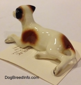 The back left side of a figurine of a brown with white and black Jack Russell Terrier dog in a lying down pose. The figurine has long legs.