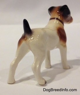 The back right side of a white with brown and black Jack Russell Terrier figurine. The figurine has long legs and it is glossy.
