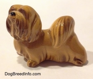 The left side of a figurine of a Lhasa Apso figurine. The figurine has a short hairy tail on its back. Its tail looks like a pom pom.