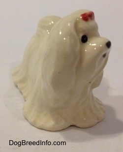 A white Maltese figurine with a red ribbon in its hair. The figurine has short legs.