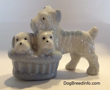 A figurine of a bone china Miniature Schnauzer dog next to a basket of her puppies. The basket is very detailed.