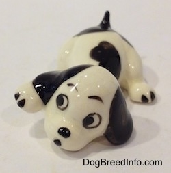 A white with black puppy figurine that is in a lying pose. The figurine has big black circles for eyes.