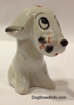 The front right side of a white with black sitting mixed breed dog figurine. The figurine has a bumblebee on its snout.