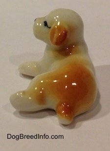 The back of a figurine of a white with brown bone china puppy figurine that is in a lying down pose. The figurine has a short brown tail.