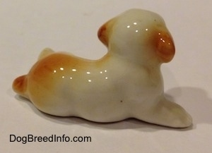The right side of a white with brown bone china puppy in a lying down pose figurine. The figurine has brown ears.