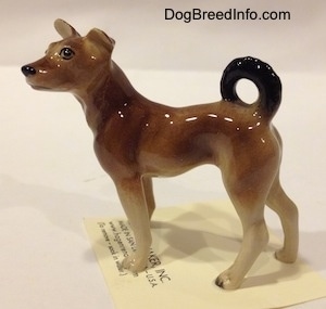 The left side of a mixed breed dog figurine. The figurines tail is curled up onto its back.
