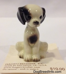 A figurine of a white with black sitting puppy.