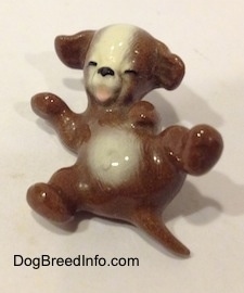 A brown with white dog figurine that is laying on its back also has its mouth painted open.